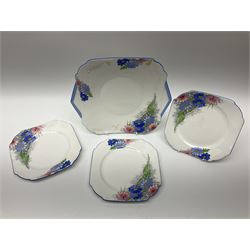 Shelley Strand shaped tea wares, decorated with blue and pink daisies upon a white ground, comprising four teacups, four saucers, three tea plates, milk jug, sugar bowl and cake plate, all with printed green mark beneath and painted pattern no 12216