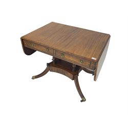 Regency period mahogany drop-leaf sofa table, rectangular top fitted with two cockbeaded drawers with ebony stringing, raised on turned columns united by quadrupod base, the sabre supports terminating in brass cups and castors