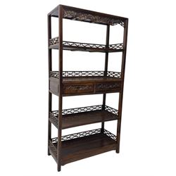 Early 20th century Chinese hardwood display étagère bookcase, the rectangular open tiered frame with pierced frieze and geometric openwork gallery to each shelf, fitted with two short drawers carved with stylised lotus motifs, supported on square uprights with pierced apron and integral gallery rails