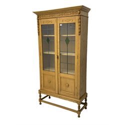 Early 20th century oak cabinet, projecting cornice over blind fret-work frieze, two glazed doors enclosing shelves, on turned supports joined by plain stretchers