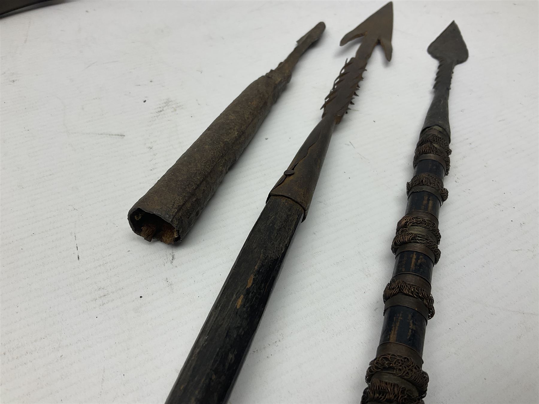 Native hand forged iron fishing spear, the V-shaped head with barbed neck and hewn haft L171cm; and two other hand forged iron spear heads, one with remains of copper bound haft (3)