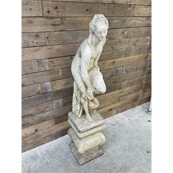 Cast stone garden statue of partially draped classical female figure on ornate pedestal 