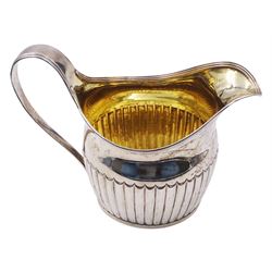 Large George III silver cream jug, of part fluted oval-helmet form, with engraved crest beneath lip, curved handle, and gilt interior, hallmarked William Bateman I, London 1816, including handle H4.5cm, approximate weight 11.20 ozt (348.6 grams)