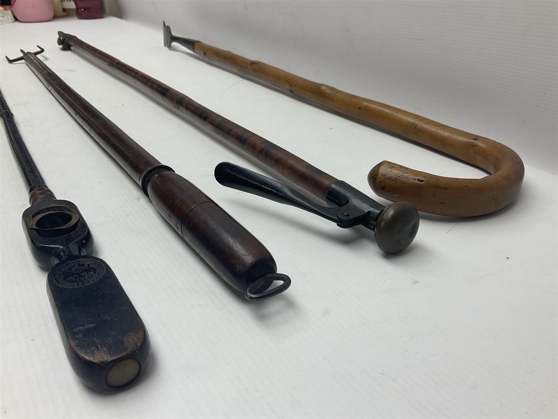 Two late 19th century fruit picker canes, the first example a French ebonised bamboo cane, with pair of fruit scissors to base, the handle stamped Cueille Fruit, the second example with grabbing action, the cap stamped A C Harris, Leicester, together with two other 19th century canes, one with fork and the other with hoe