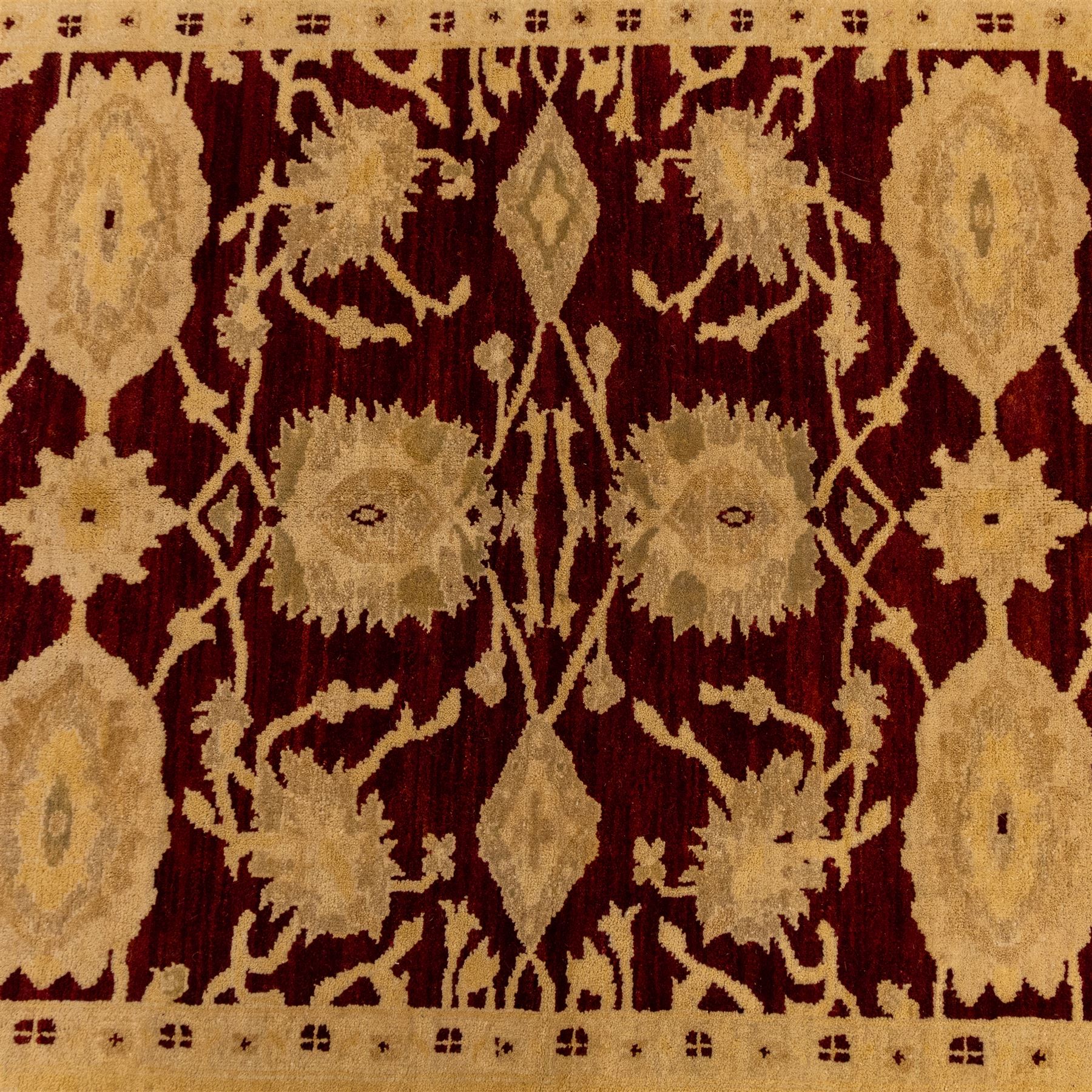 Ziegler design hand knotted wool rug, the rich red ground woven with oversized floral medallions and angular vine scrolls, framed by a contrasting ivory border of repeating floral ornament and minor guard stripes, with fringed ends
