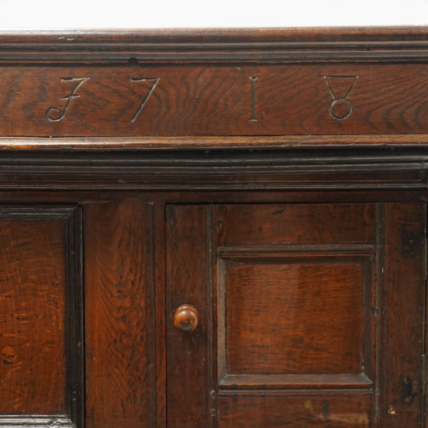 Early 18th century oak court cupboard, the projecting cornice carved with initials 'WKIW' and dated 1718 with turned terminals, fitted with two recessed panelled cupboard doors, large cupboard to base, raised on stile supports