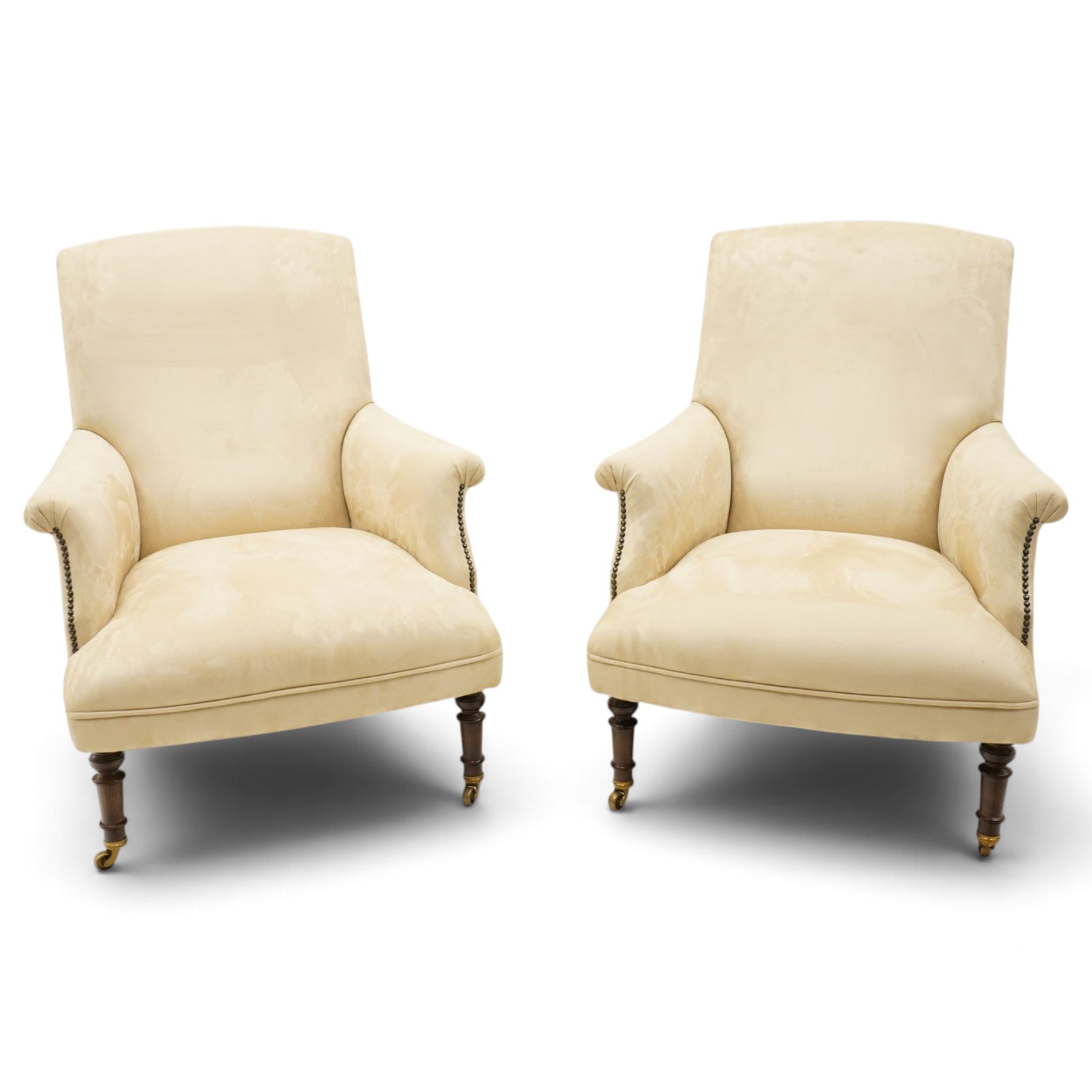 Sofas & Stuff - pair of ‘Thistle’ armchairs upholstered in neutral fabric, each with gently sloping back, padded scroll arms with close-set stud detailing, loose seat cushions, raised on turned wooden legs with brass castors