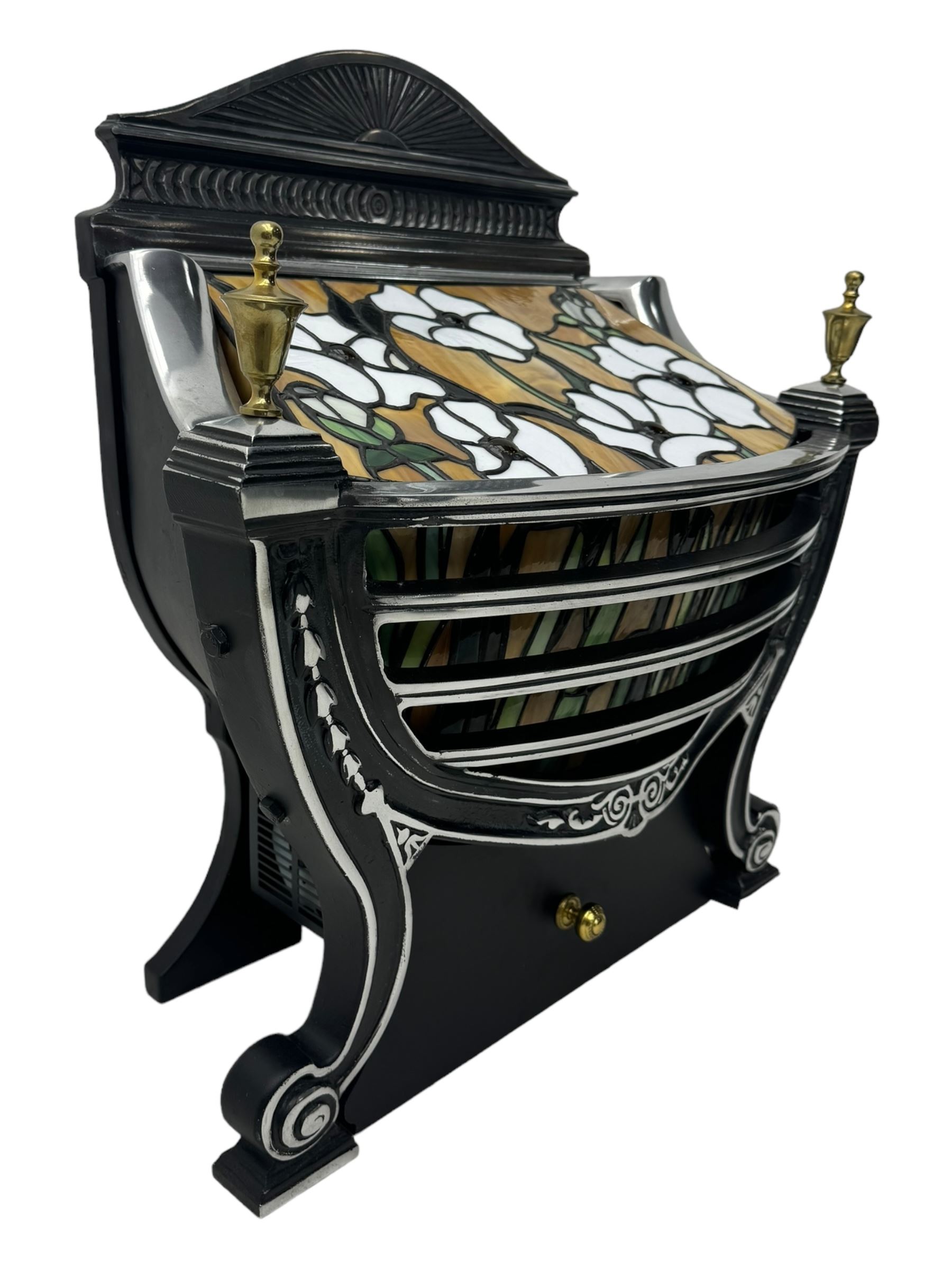Stained glass and cast iron electric fireplace, arched top with decorative finials, stained glass front panel with floral motifs, flanked by cast iron scrolls, raised on scroll supports