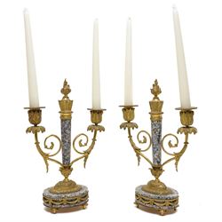 French- early 20th century portico clock garniture, 8-day drum movement decorated with laurel leaves to the glazed bezel and surmounted by a decorative urn with scroll handles, raised by four matching columns on a granite effect oval base with toupee feet, convex enamel dial with gilt pierced hands, Arabic numerals, minute markers and a garland of flowers, twin train Parisian rack striking movement, striking the hours and half hours on a bell. With a sunburst pendulum and key and a matching pair of two-light candelabra.