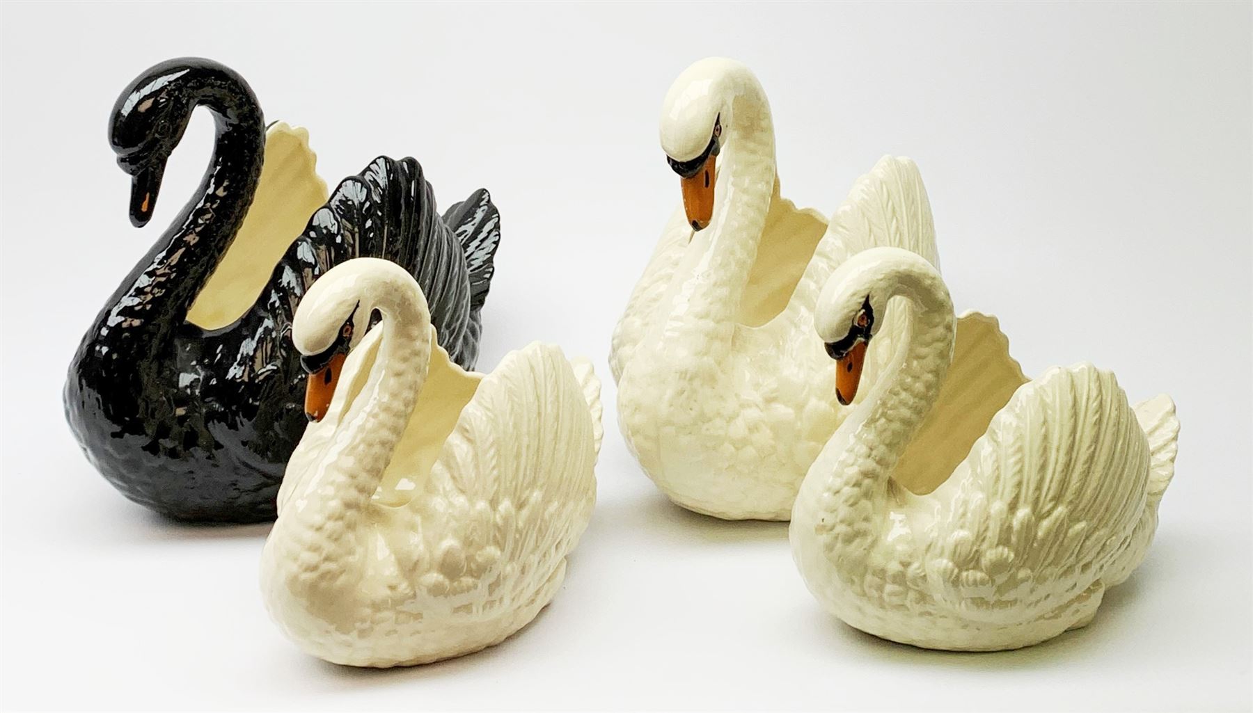 Four Dartmouth pottery jardinières or planters, modelled in the form of swans, comprising three white examples, and one black, marked beneath Dartmouth Devon England, larger examples H29cm, smaller examples H21.5cm. 