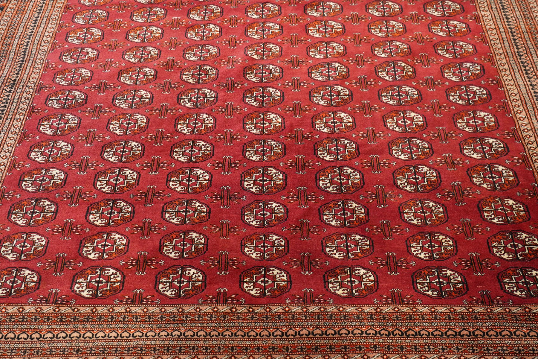 Large Afghan Bokhara crimson ground carpet, the field with rows of repeating Gul motifs and geometric design, enclosed by multiple repeating geometric guard bands