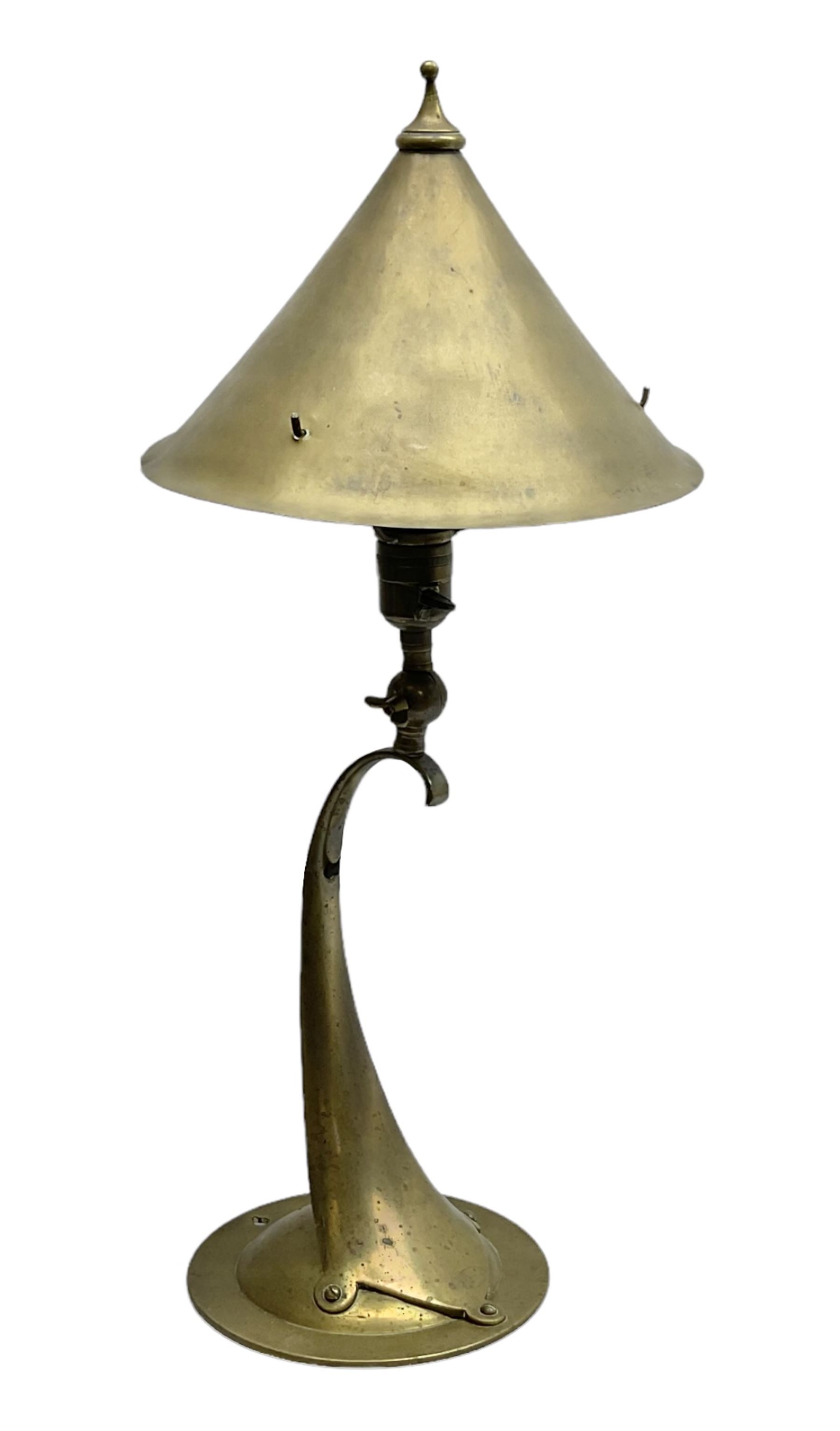 Arts & Crafts Jesson, Birkett & Co, brass table lamp or wall light, designed by Thomas Birkett, the tapering stem with adjustable ball pivot supporting a conical shade with tapering final with ball terminal, upon a circular domed base pierced for wall mounting, shade positioned upright overall H57cm

Often misattributed to Arthur Stansfield Dixon for Birmingham Guild of Handicraft, this particular lamp was designed by Thomas Birkett.
In the late 1890's Birkett worked as a metalwork at the Birmingham Guild, before later joining the Faulkner Bronze Company which went on to become Jesson, Birkett & Co in 1904. The lamp features in lighting catalogues from the firm under the model no E490.

