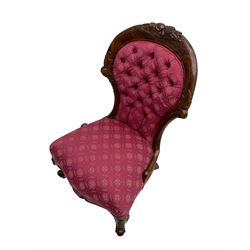 Victorian style mahogany framed nursing chair, the cresting rail carved with fruit and foliage, upholstered in red patterned fabric with buttoned back, on cabriole supports with scrolled terminals