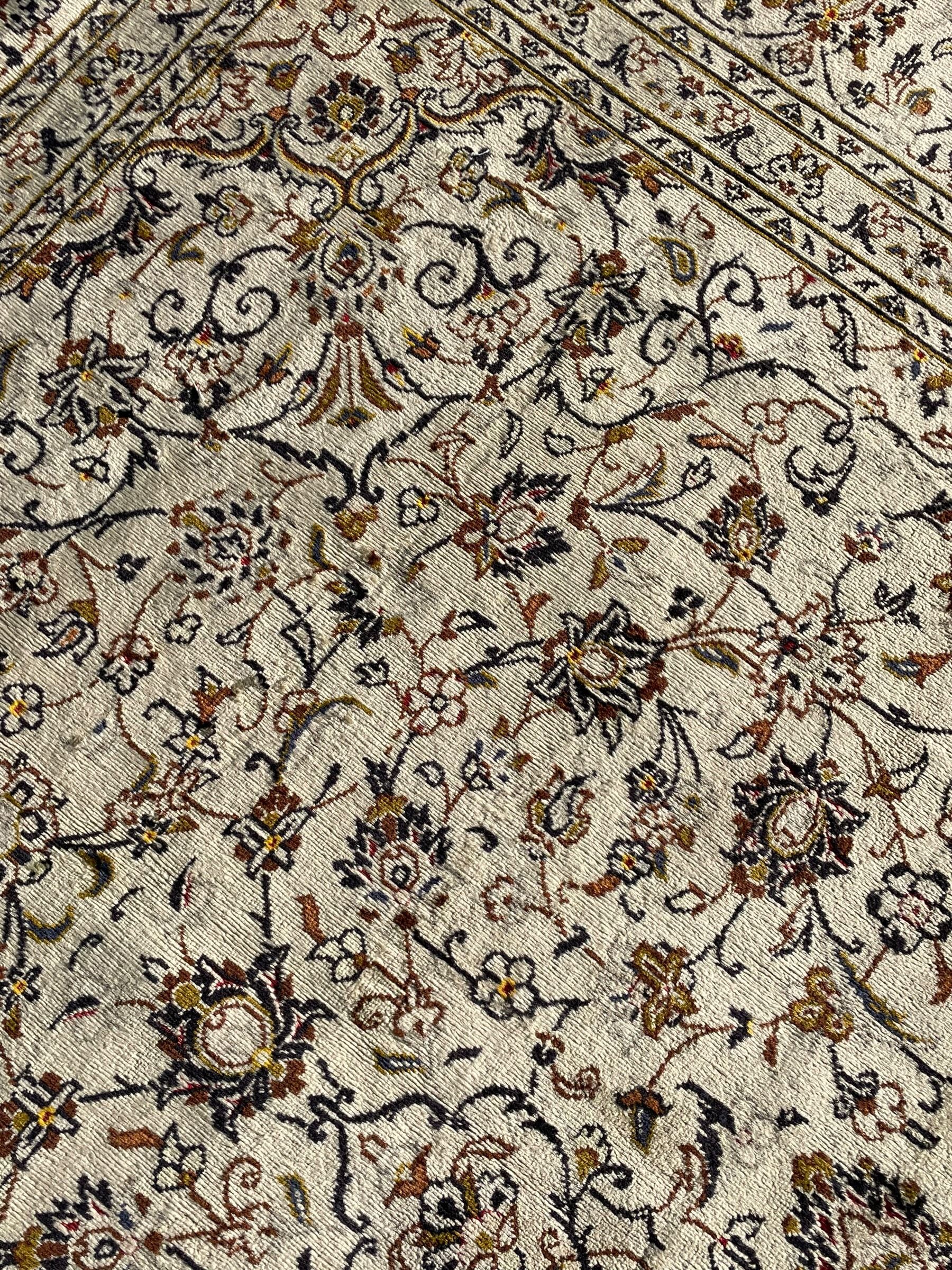 Persian Kashan ivory ground carpet, central medallion decorated with sixteen arranged palmette motifs, within a field decorated with swirling leafy branches and stylised plant motifs, the main border decorated with matching swirling pattern, within floral pattern guard stripes 