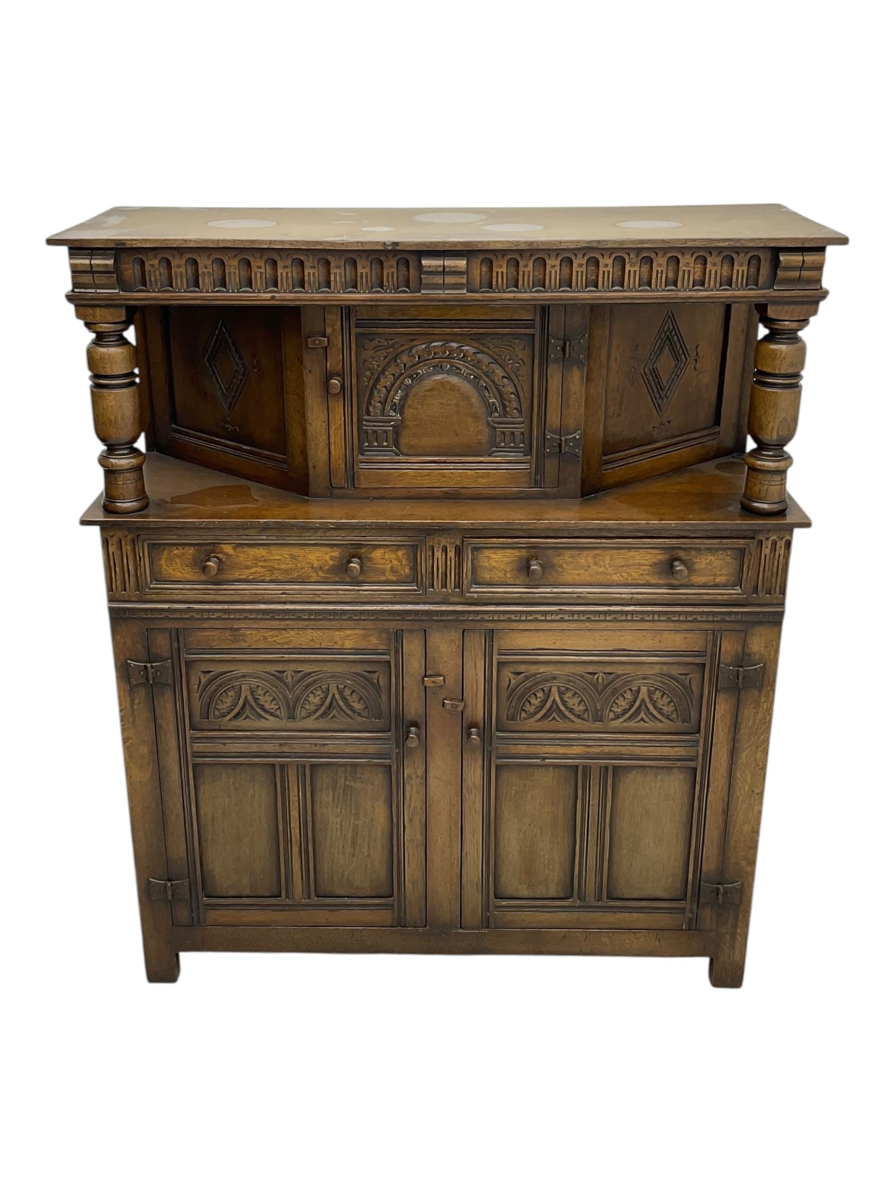 Jacobean design oak court cupboard, upper section with carved arched panelled cupboard door flanked by turned columns, beneath carved and moulded frieze, lower section fitted with two drawers over two cupboard doors with gothic arched panel decoration, raised on stile supports