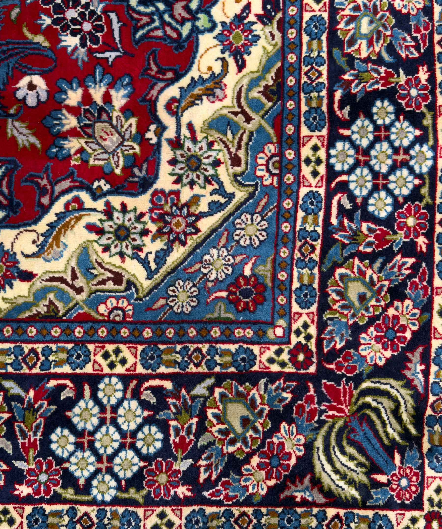 Central Persian Isfahan Carpet, hand-knotted, featuring a bold central rosette medallion on a rich red field, flanked by stylised floral sprays, scrolling foliage and mythical animals, within a broad indigo border decorated with alternating cartouches and flowerheads