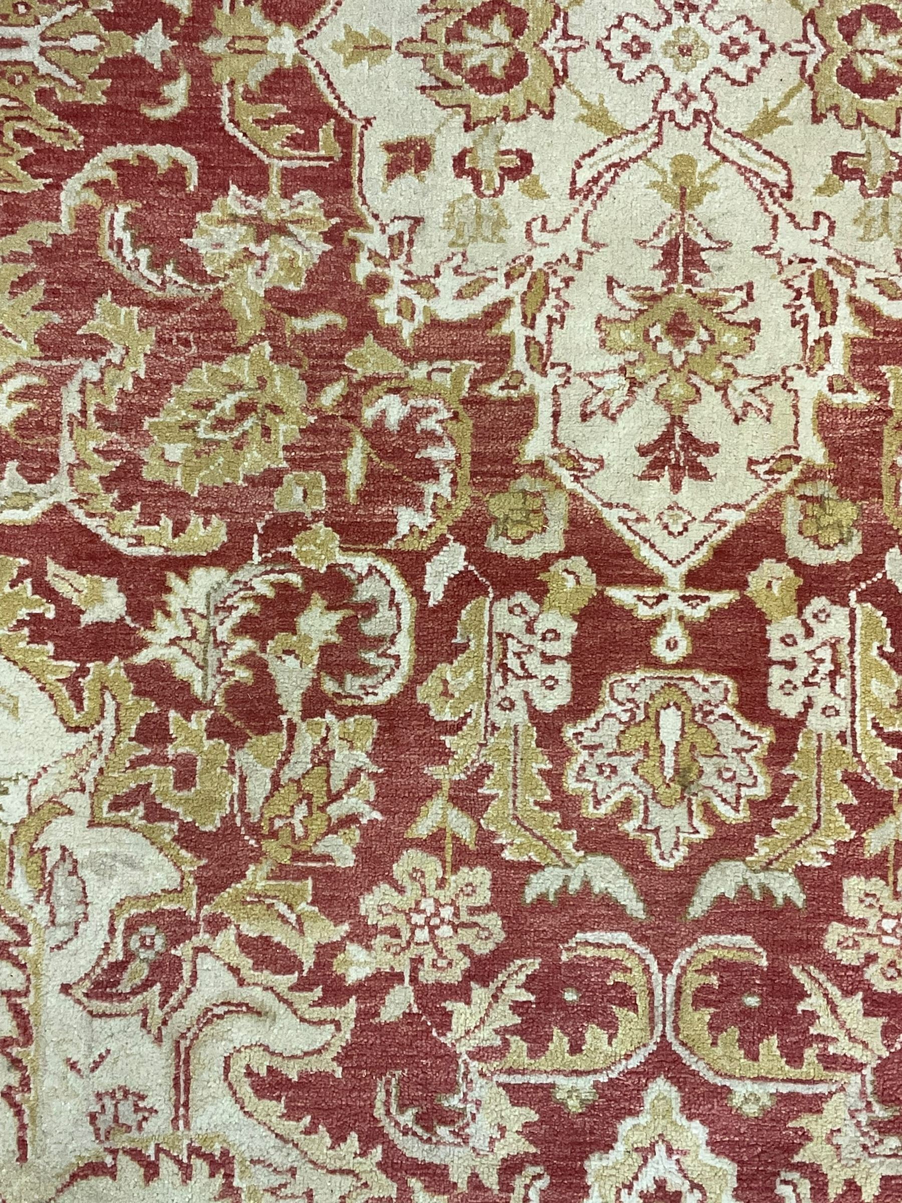 Persian design beige and crimson ground rug, the field decorated with interlacing scrolled foliage, repeating border within guard stripes 