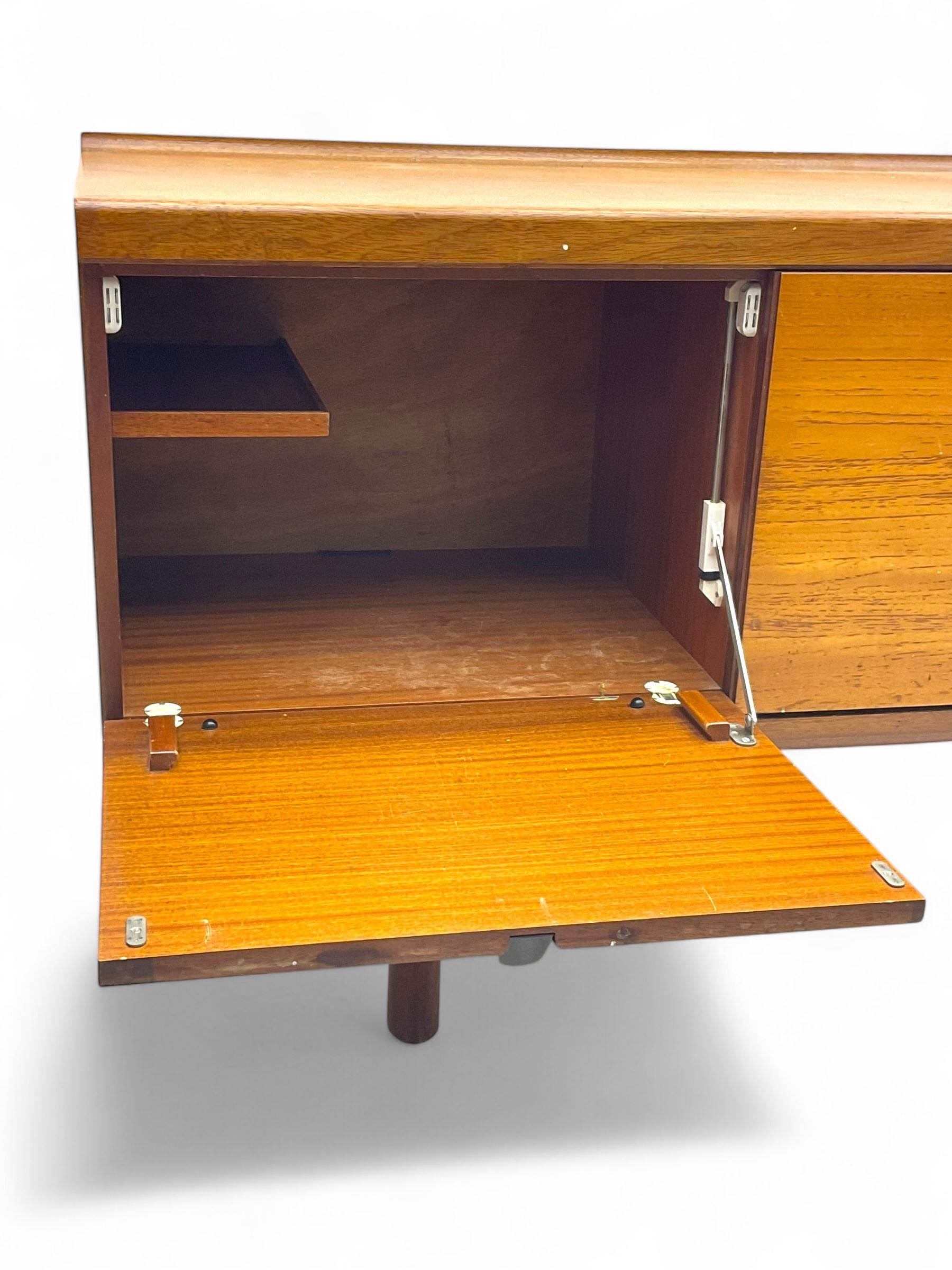 White & Newton - mid-20th century teak sideboard, rectangular top with raised back over fall-front storage compartment, double cupboard and three drawers, raised on cylindrical supports
