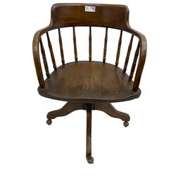 Early 20th century oak framed swivel Captain's chair, tub shaped back with turned spindle supports over saddle shaped seat, quadriform base on castors