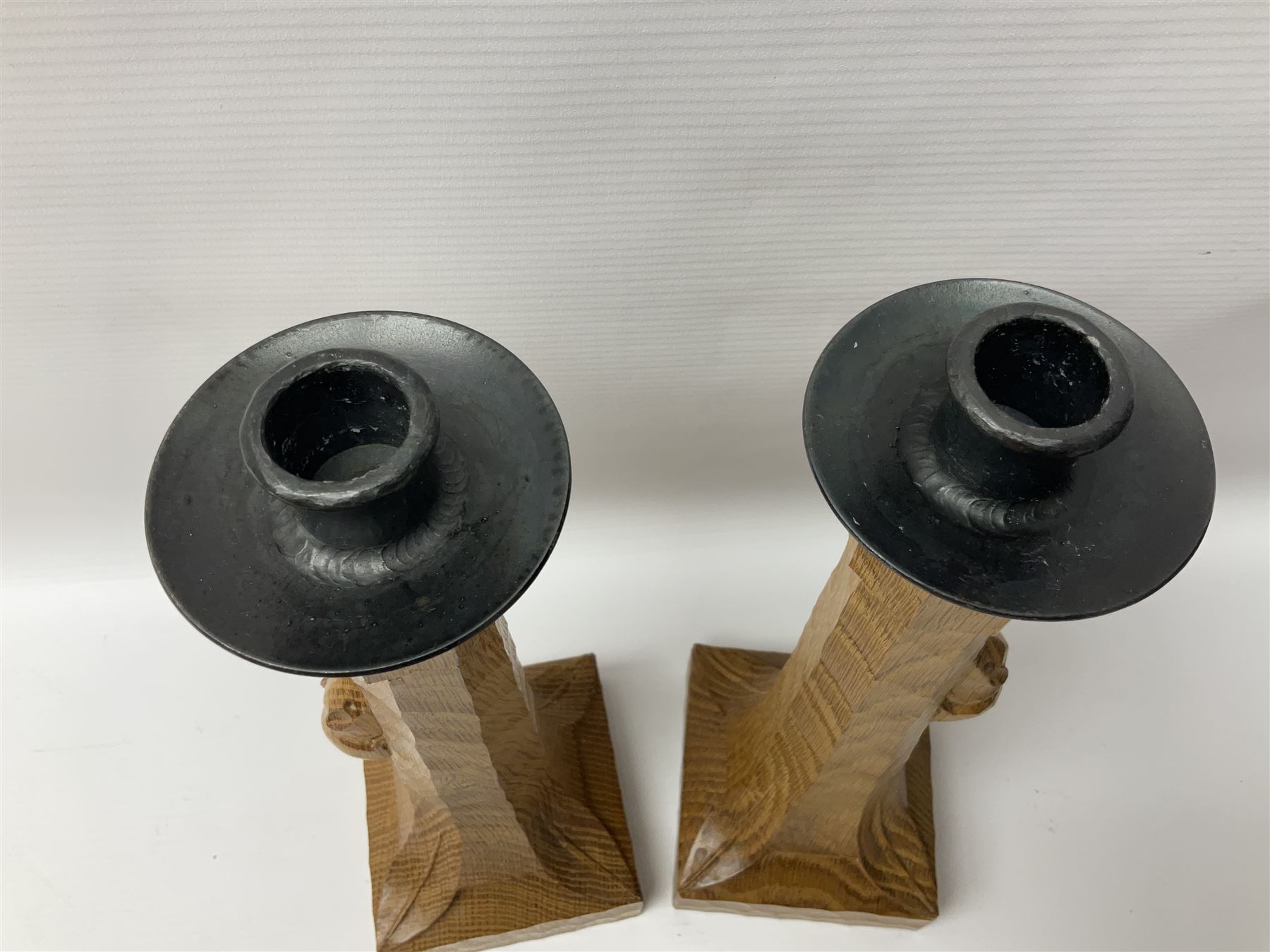Mouseman - pair of tooled oak candlesticks, wrought iron sconce with drip tray over tapered octagonal column carved with mouse signature, terminating to stylised leaf carved square base, by the workshop of Robert Thompson, Kilburn
