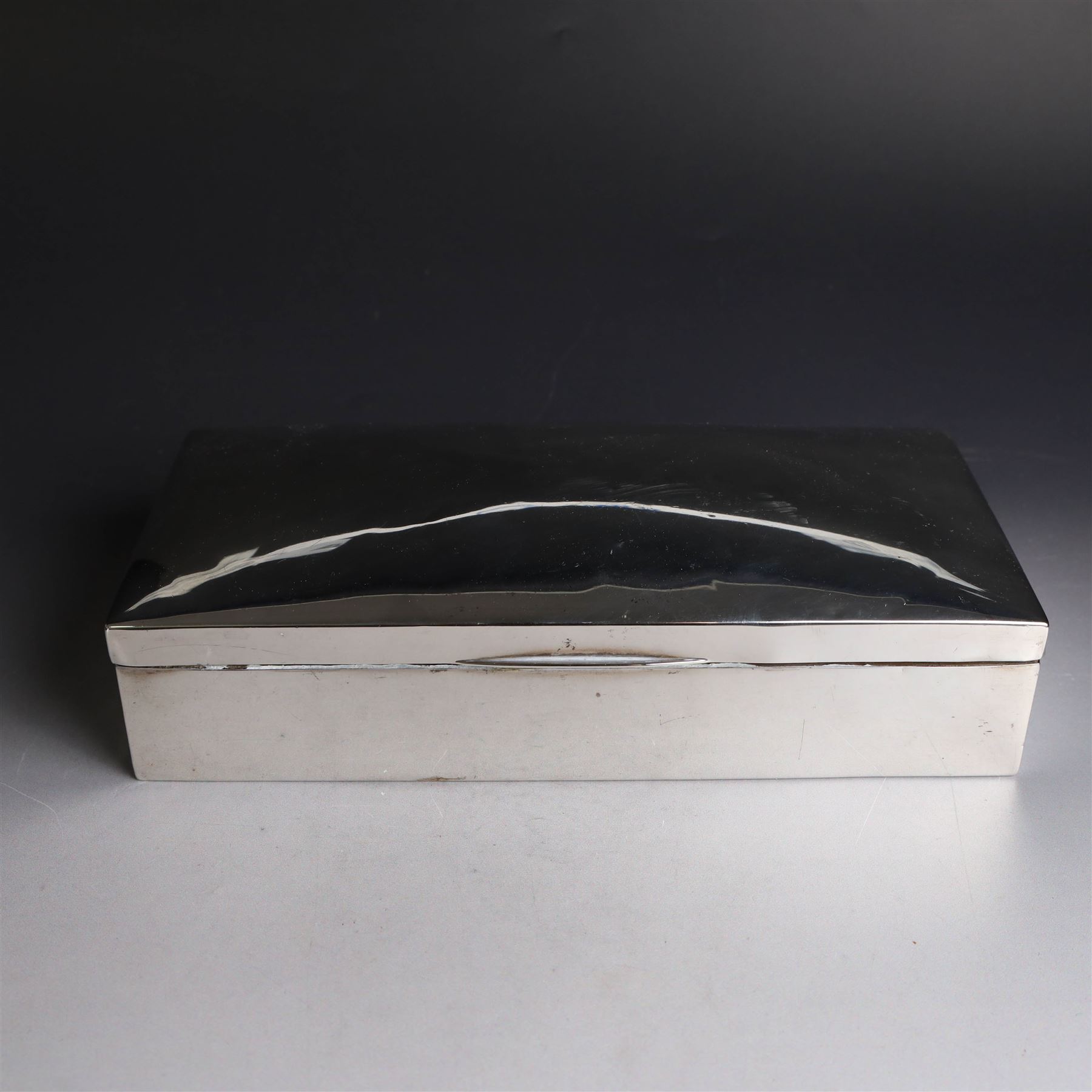 Two silver cigarette boxes, comprising early 20th century plain rectangular example with compartmentalised softwood interior, hallmarked Birmingham 1914, maker's mark indistinct, and an early 20th century example with engine turned decoration and engraved initials to cover, hallmarks worn and indistinct, largest H4.5cm, W21cm