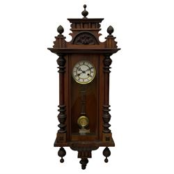 A late 19th century German wall clock with an 8-day spring driven movement striking the hours on a coiled gong, in a mahogany case with a shaped pediment and turned columns flanking a full-length glazed door, with a two-part dial enamel with Roman numerals, minute track and pierced gothic designed hands, gridiron pendulum and beat plate. With Key.




