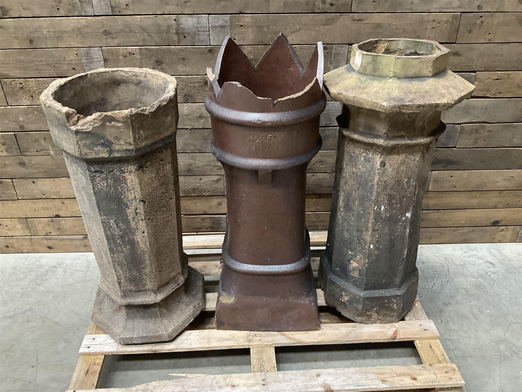 Collection of three Victorian and early 20th century reclaimed terracotta chimney pots, comprising: one cylindrical form with weathered, cracked glaze and flared octagonal base; one deep red cylindrical pot with fluted midsection and castellated rim, bearing moulded number ‘25’; and one tapering hexagonal example with wide flared rim and weathered patina. All with age-related wear and chips, consistent with use and outdoor exposure. Plus a selection of cast stone pieces including fountain 