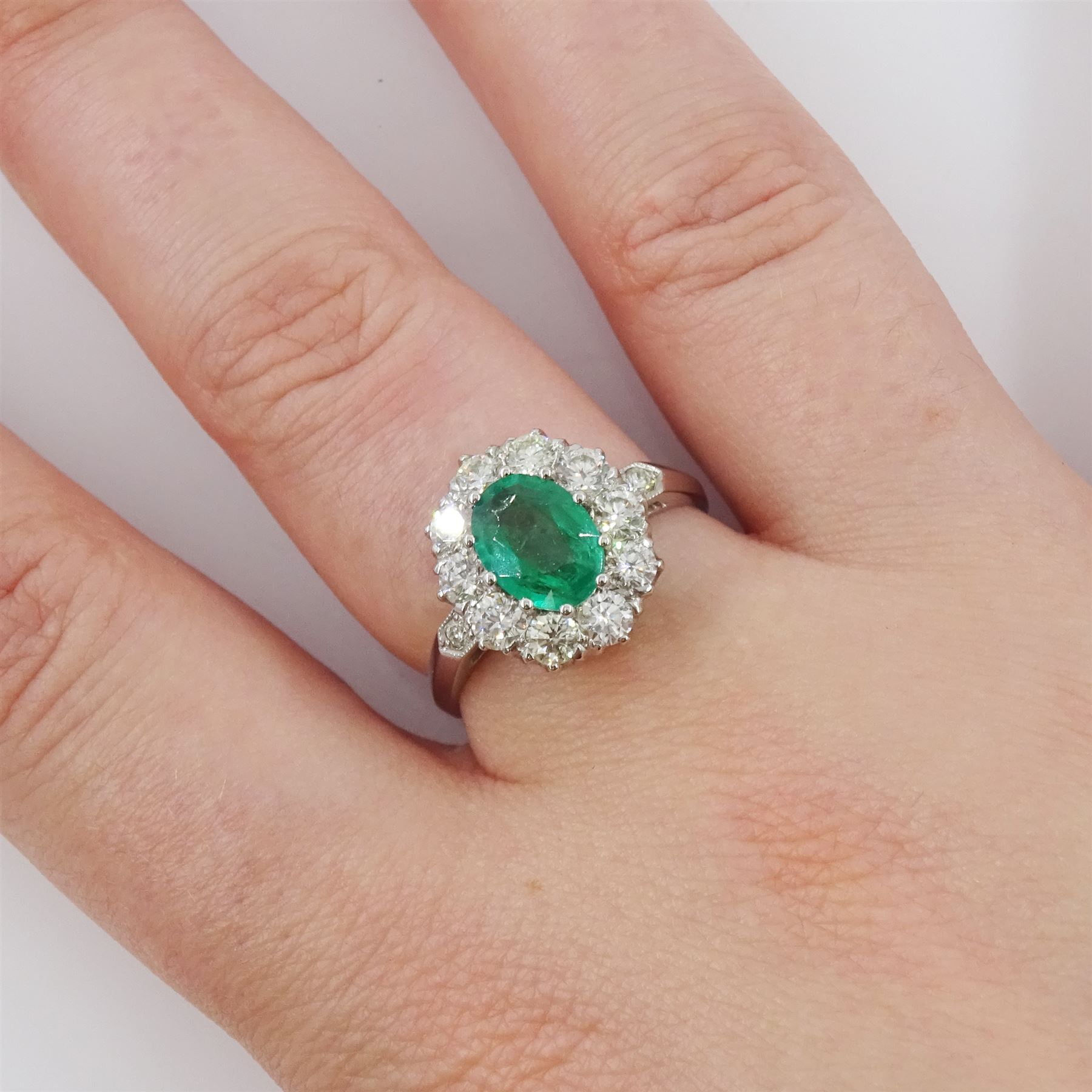 Platinum emerald and diamond cluster ring, single oval cut emerald of approx 0.90 carat, surrounded by ten round brilliant cut diamonds, and milgrain set diamond shoulders, stamped Plat, total diamond weight approx 1.00 carat