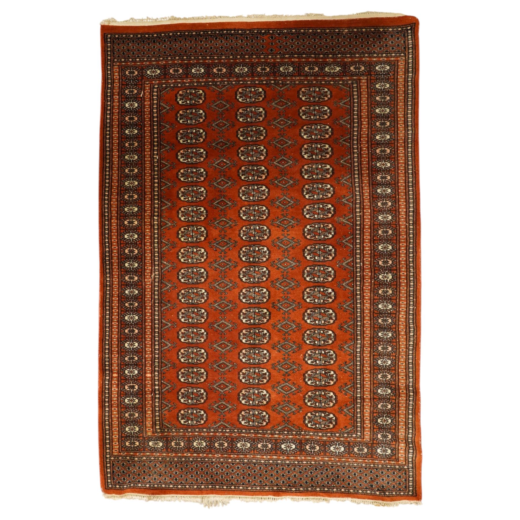 Bokhara hand-knotted carpet, terracotta ground with repeating rows of Tekke guls interspersed with geometric motifs, enclosed by multiple stylised floral and geometric borders, with fringed ends