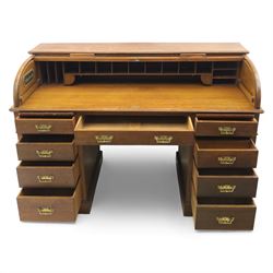 Edwardian oak roll-top desk, the tambour enclosing a fitted interior of pigeonholes and dividers, over a central kneehole flanked by twin banks of drawers with brass handles, on plinth bases
