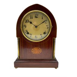 A late 19th century American  mantle clock in a “Lancet” case manufactured by the  Gilbert Clock Factory, Connecticut,  mahogany veneered case with an oval inlay, satinwood stringing to the edge and two recessed brass pillars, on a moulded plinth with four bun feet, enamel dial with upright Arabic numerals and spade hands, fast/slow regulation, with a convex glass and spun brass bezel, eight-day movement striking the hours and half hours on a coiled gong. No pendulum.