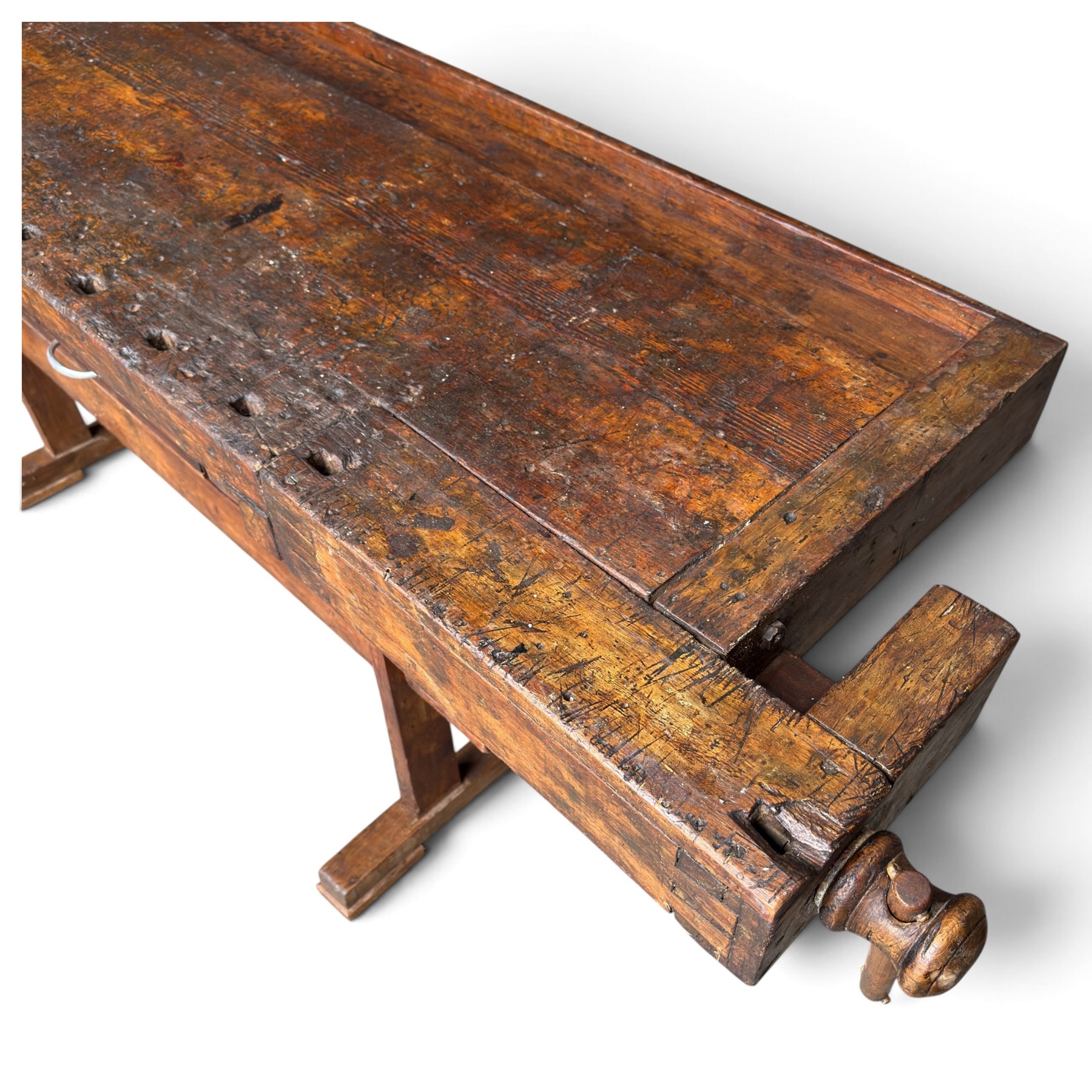 Large early 20th century rustic stained reclaimed pine workbench, the substantial plank top with recessed tool well and two homemade wooden screw vices, above a single frieze drawer and slatted undertier, raised on trestle end supports