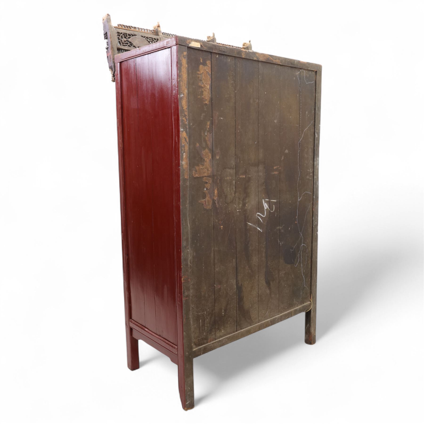 Early 20th century Chinese lacquered marriage cabinet, of rectangular form in red lacquer, fitted with double doors centred by circular brass lock plate and drop handles, the interior with shelves and two short drawers, cornice and apron with giltwood foliate and figural carving, together with an elaborately pierced and gilded wooden cresting panel carved with scenes of figures within pavilions and stylised dragons