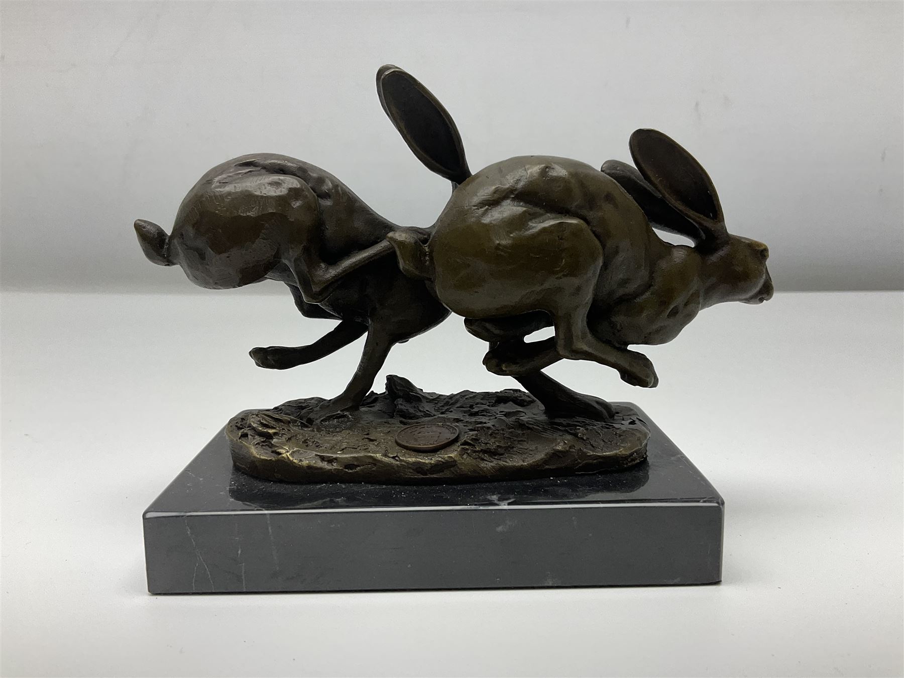 Bronze figure group, modelled as two hares in chase, upon a naturalistic base signed Nick and with foundry mark, raised upon a rectangular marble base, overall H12cm. 