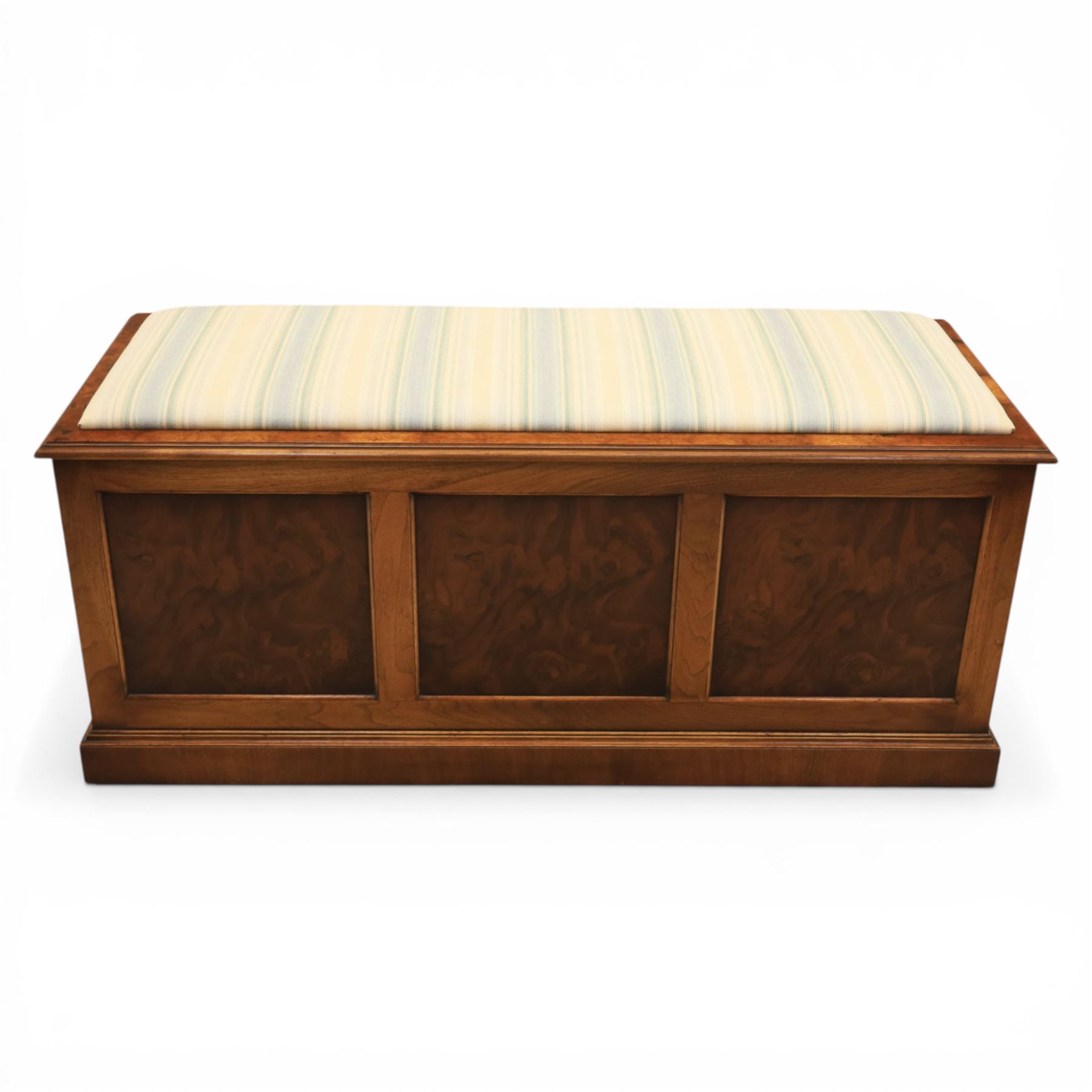 Traditional design figured elm blanket chest, with padded striped upholstered seat, over a hinged top with panelled sections below raised on a plinth base