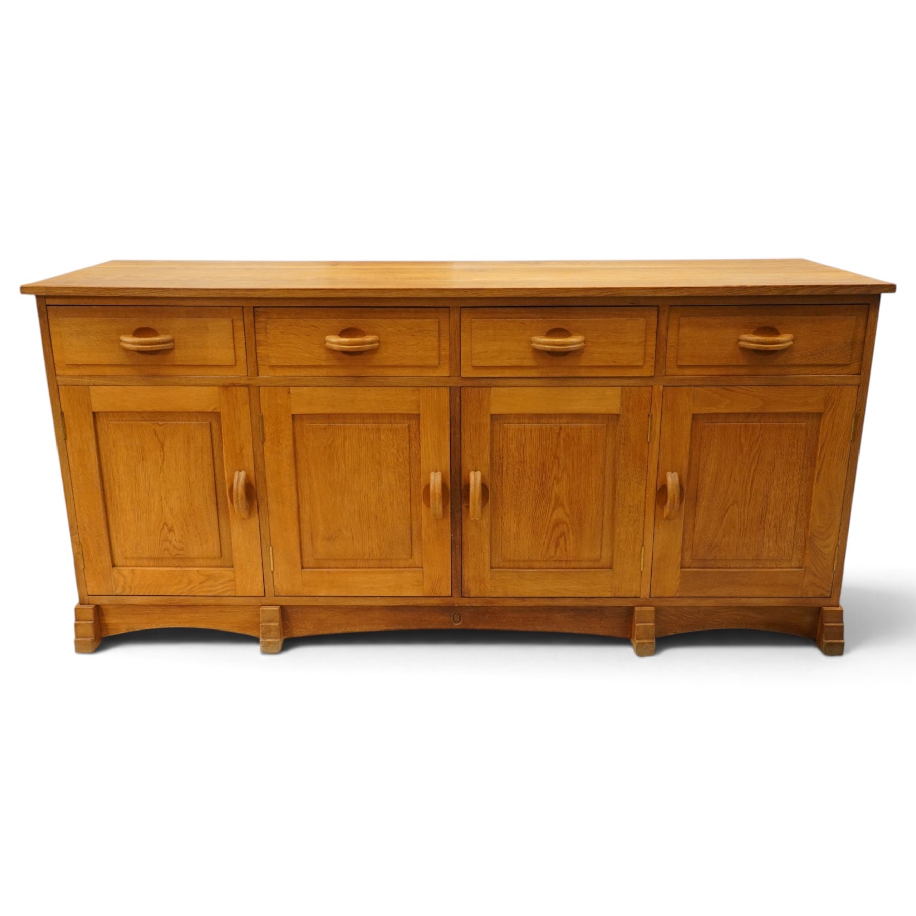 Acorn Industries - oak dresser base or sideboard, the rectangular top over three drawers with protruding oak handles, over four panelled cupboard doors enclosing a single shelf, raised on stepped feet, carved with acorn signature, by Alan Grainger, Brandsby