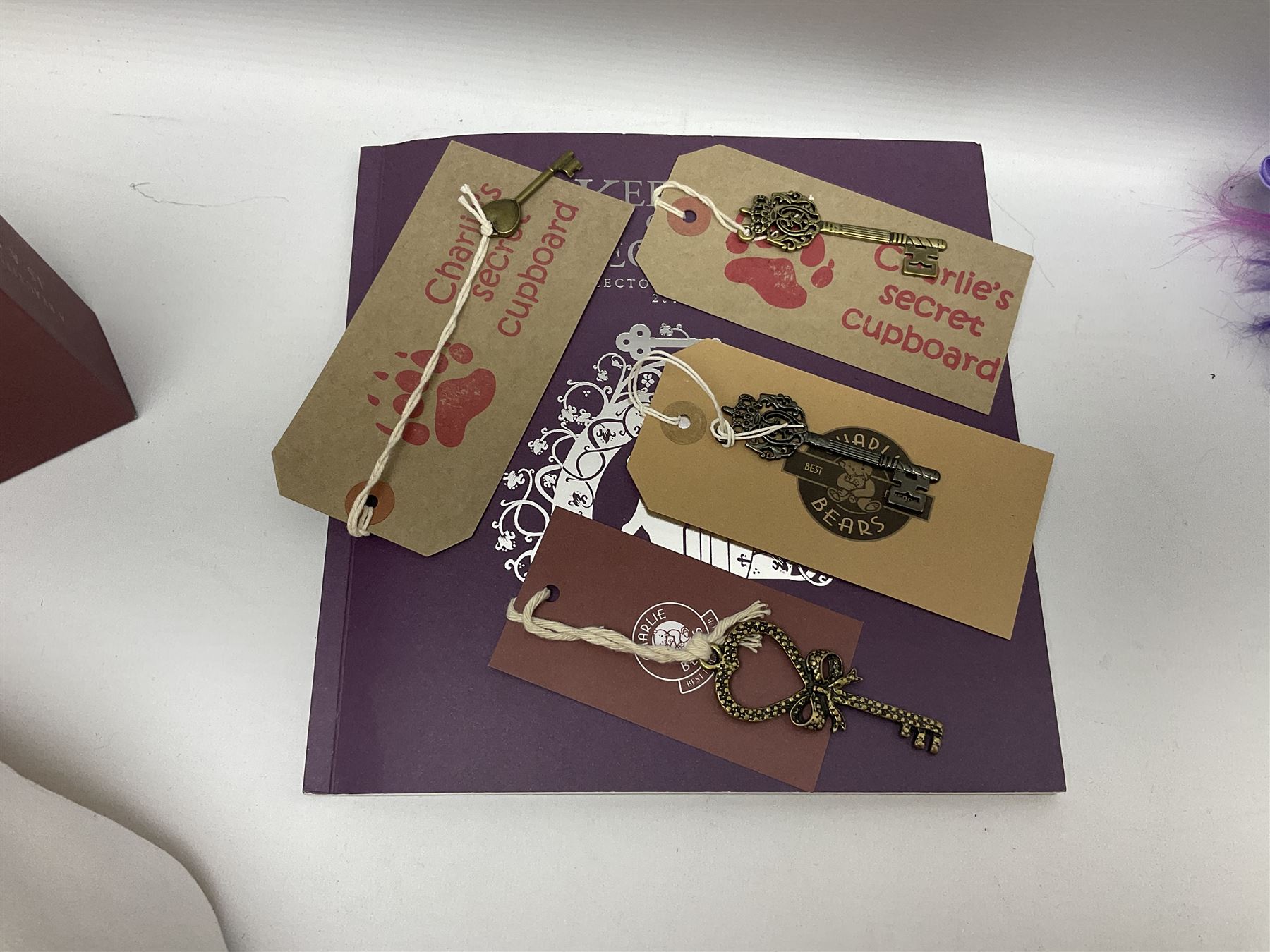 Five Charlie Bears Plush Hug Book Collection books, comprising Guide To Snuggleability containing Snuggleability CB191971F, Paw-Some Facts Directory containing Pawsome CB191971D, Bear Therapy Handbook containing Bear Therapy CB191971E, Study Buddy Handbook containing Study Buddy CB191971A, and Guide to Being Bear-illiant CB191971B, each designed by Isabelle Lee, each with tags, plus Charlie Bears Secret Hug Book (lacking contents), together with assorted Charlie Bear accessories, to include two Bear Ears Duffle headbands CBBEARSDUF, Egg Cup CB185198 , Incy Wincy CB205252AO, with tag, four key rings, all with tags, Bear Care Kit and contents, recipe cards, pin badges, tape measure, notebook, etc., (Qty)