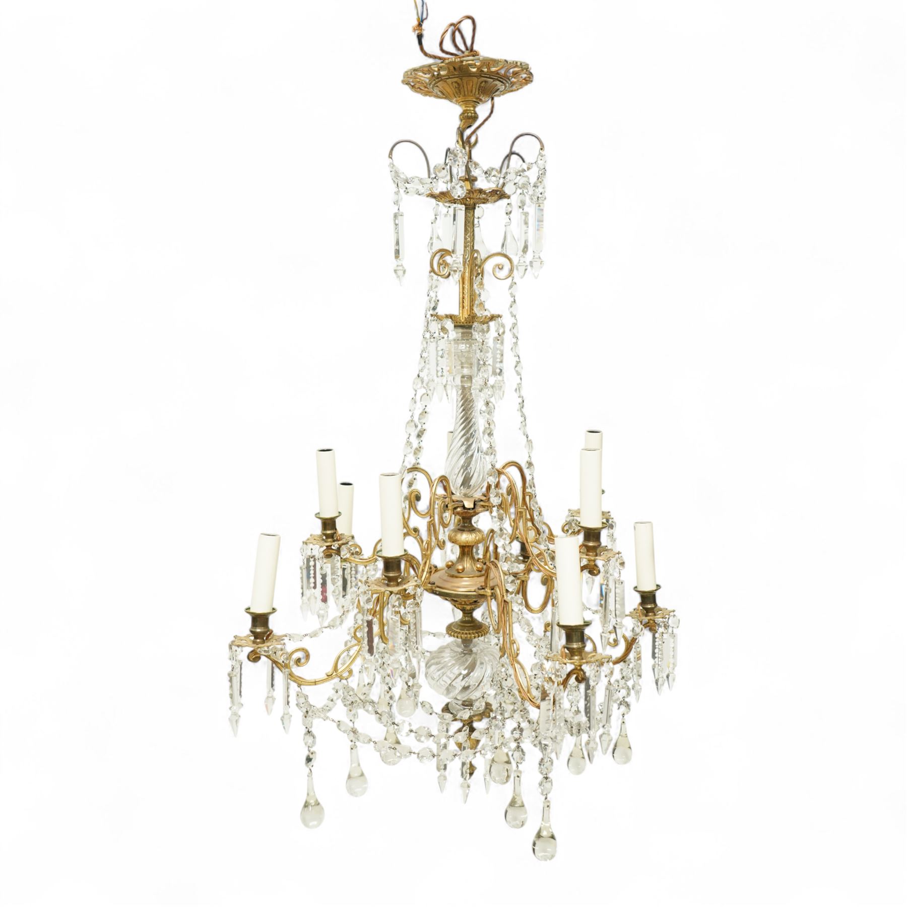 Late Victorian gilt bronze mounted crystal chandelier, ceiling rose above shaped top of trailing swags, glass crystal droplets, beneath rising curled branches and glass beads tapering down to five candle sconces, inside circular bezel fitted with drops and glass twist fluted stem, supported with an internal metal shaft above a rococo style stem holding double branches, and similar styled branches, with twelve branches fitted with candle holders and drip trays with crystal drops and cut crystal spears, the underside festooned with crystal glass swags and a bulbous fluted glass terminal and shaped finial with crystal glass swags attached to the branches, the base with pear shaped droplet graduating to the centre, wired for electricity 