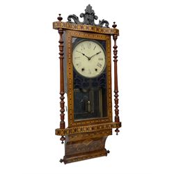 A late 19th century spring driven American Eight-day wall clock, striking the hours on a bell, in a parquetry case with contrasting oak, maple, walnut, and other hardwoods, with a flat top, carved cresting and finials rectangular glazed door flanked by finely turned pilasters, with a painted dial with roman numerals and minute track, steel spade hands and faux mercury pendulum reflected in a rear case mirror.   


