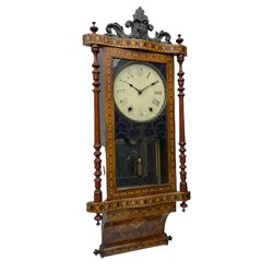 A late 19th century spring driven American Eight-day wall clock, striking the hours on a bell, in a parquetry case with contrasting oak, maple, walnut, and other hardwoods, with a flat top, carved cresting and finials rectangular glazed door flanked by finely turned pilasters, with a painted dial with roman numerals and minute track, steel spade hands and faux mercury pendulum reflected in a rear case mirror.   


