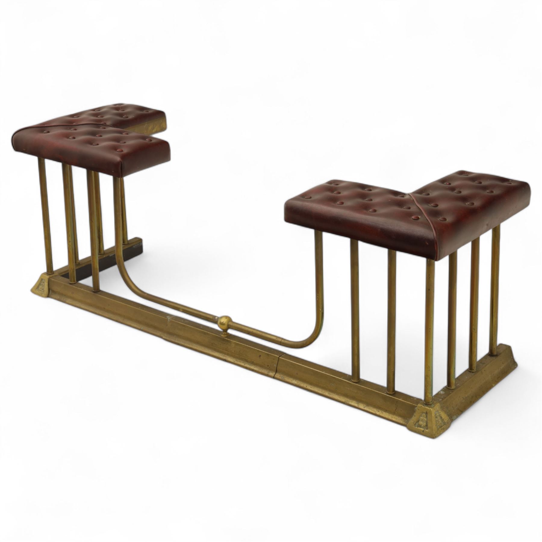 Late Victorian brass and cast iron club fender, burgundy leather buttoned seat pads, secured by bar uprights at the front and back, and a cross stretcher held in place by further bar uprights on a chamfered platform base, circa 1890, internal base dimensions 127cm 