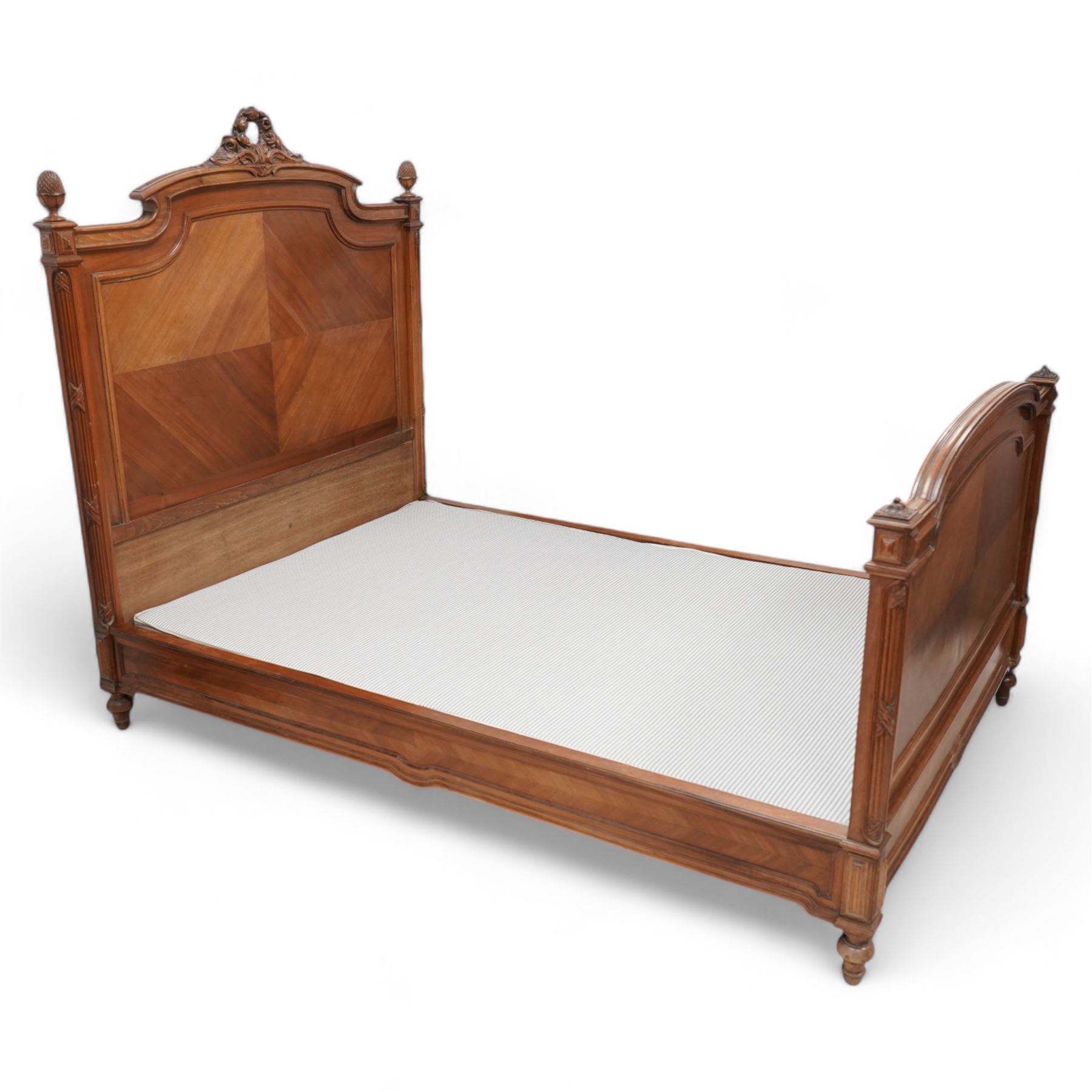 20th century French walnut 4' 6'' double bedstead, the headboard with flower head wreath pediment flanked by carved pineapple finials, reed and ribbon carved corner uprights, quarter-matched veneers, on turned feet, together with upholstered bed base