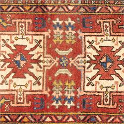North west Persian Heriz runner, madder red field with a single column of alternating hooked and stepped lozenge medallions in ivory, blue, and terracotta, scattered with small cruciform and geometric motifs within a brick red border, angular motifs between narrow guard stripes 