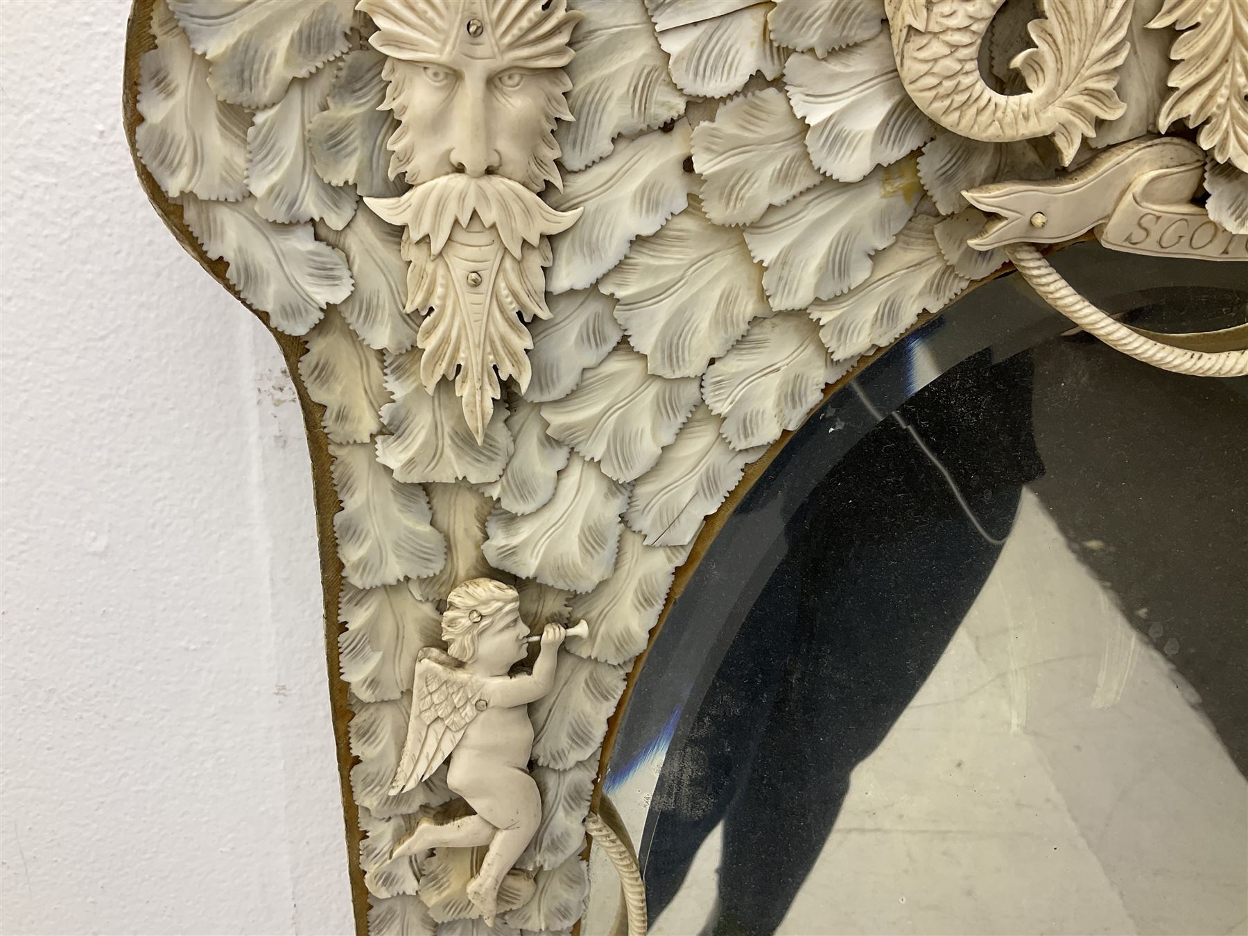 Pair 19th century French Dieppe bone and ivory wall mirrors, the oval bevelled mirror plates within rectangular frames with shaped tops, profusely decorated with ivory leaves, further detailed with carved bone armorial type crest inscribed 'SGOTORVM', putti, fish and mask heads, H81cm W48cm