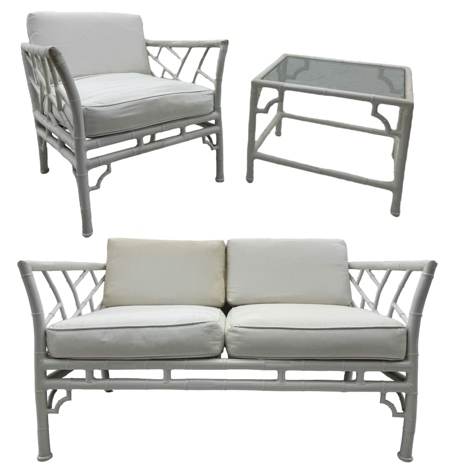 Late 20th century faux bamboo conservatory sofa, white painted frame with geometric openwork back and sides, loose cream cushions, on cylindrical supports (W134cm, D76cm, H80cm); matching armchair (W75cm, D76cm, H80cm); matching coffee table with glass insert (W46cm, D45cm, H36cm)
