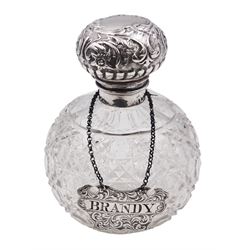Victorian silver wine label for Brandy, of shaped form with engraved foliate detail, hallmarked George Unite, Birmingham 1859, together with a late Victorian/Edwardian silver mounted cut glass scent bottle, the glass body of spherical form with octagonal and hobnail cut decoration, the hinged silver cover embossed with flower heads and scrolls, opening to reveal an internal glass stopper, hallmarked Walker & Hall, Sheffield, date letter worn and indistinct, H13.5cm