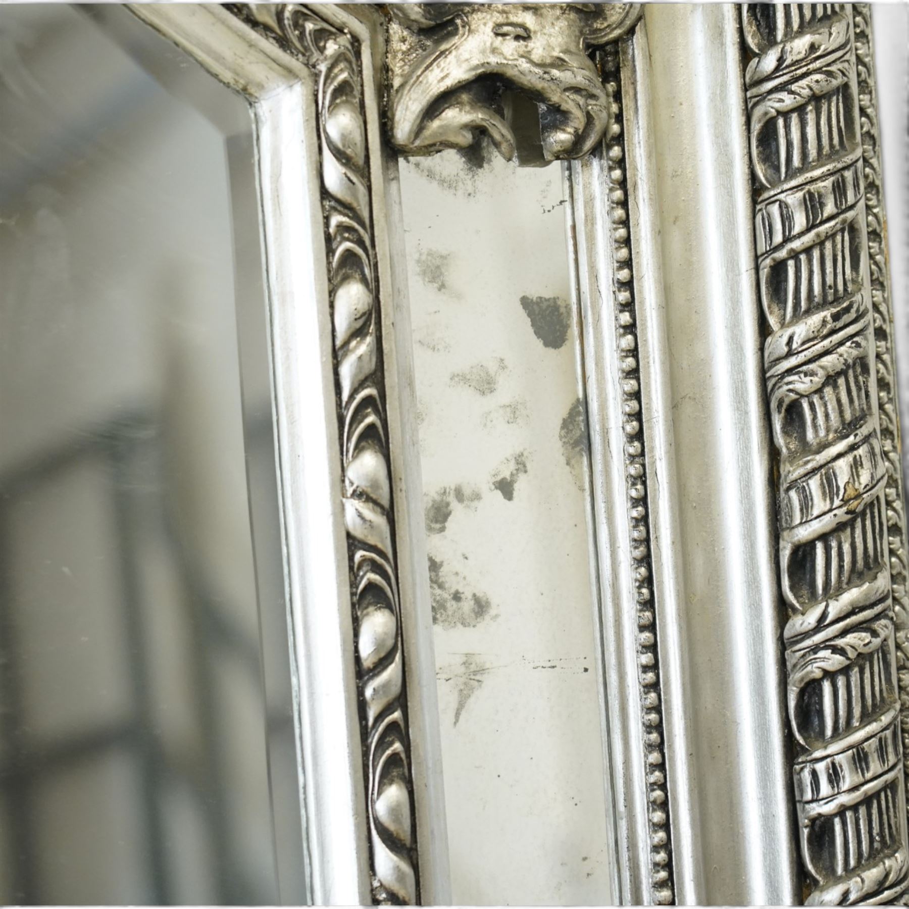 Impressive Baroque Revival mirror in antique silvered finish, the pierced cartouche shell pediment flanked  by C-scrolls and flower heads, the outer frame with ribbon-twist motifs throughout, the central arched bevelled plate surrounded by further rectangular mirror panels with cartouche mounts