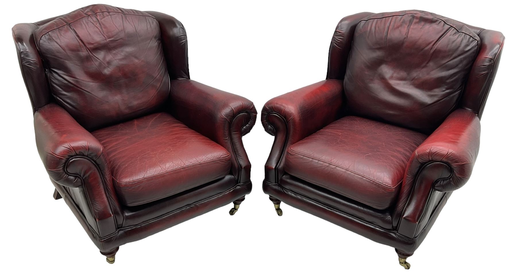 Thomas Lloyd - three-piece lounge suite, comprising of traditional shape two seat sofa (W190cm H80cm) and a pair of wingback armchairs (W100cm H91cm), each with rolled arms over turned supports with brass castors, upholstered in oxblood red leather
