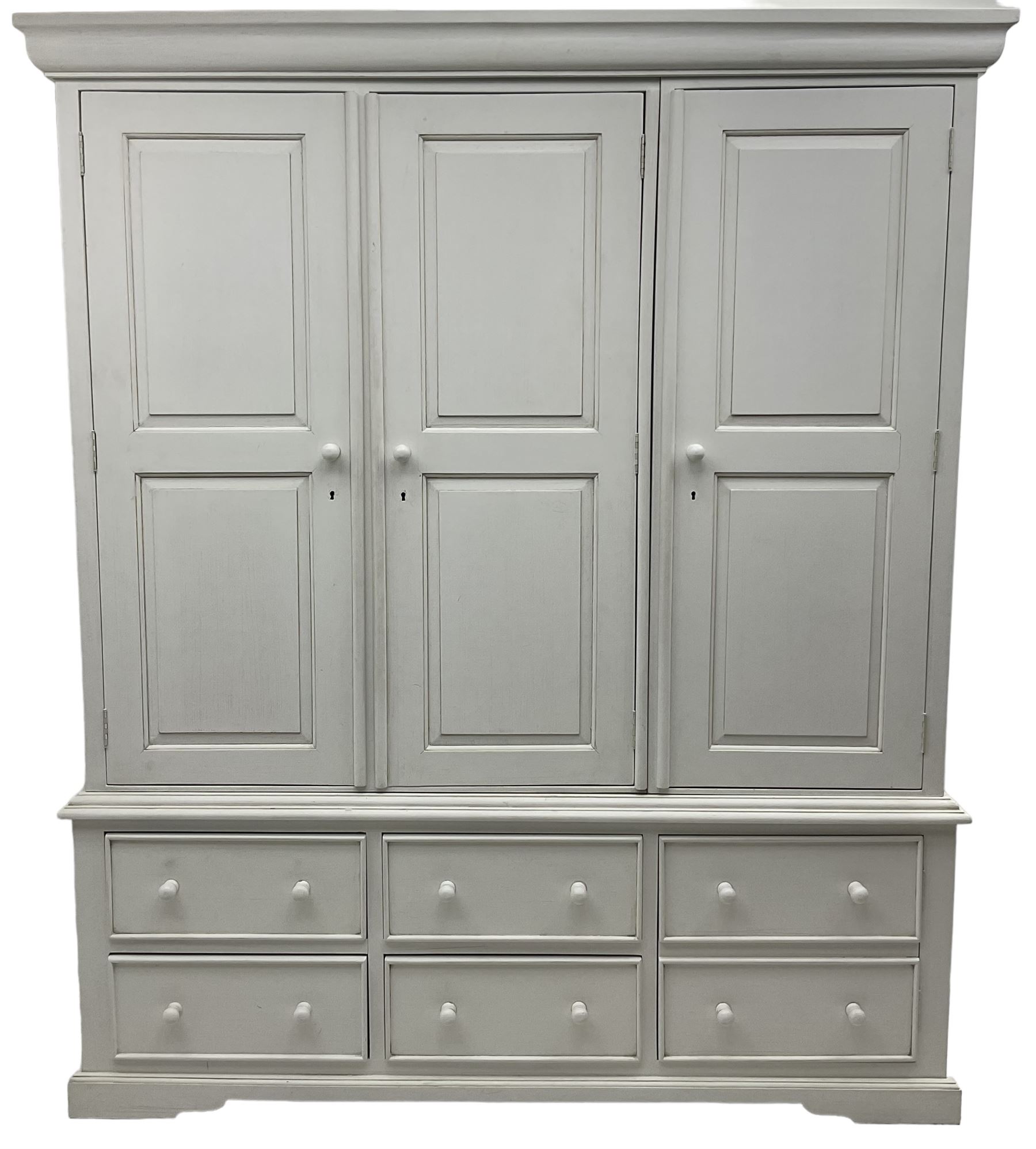 White painted triple wardrobe, projecting moulded cornice over three panelled doors, the interior fitted with hanging rails, four drawers and hinged cupboard to base, on bracket feet