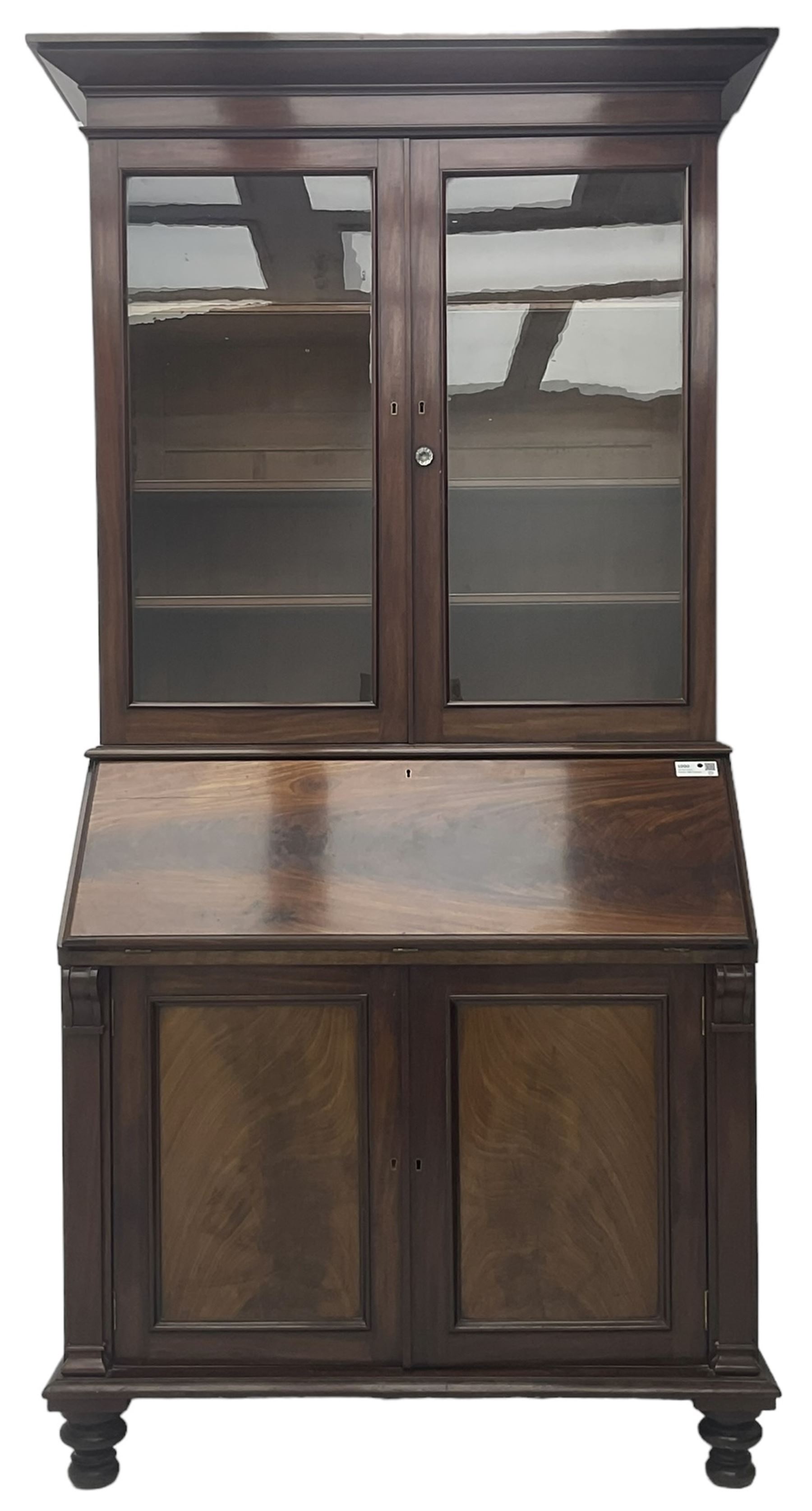 Early 19th century figured mahogany bureau bookcase, projecting splay moulded cornice over three adjustable shelves enclosed by two glazed doors, fall front revealing pigeonholes, cupboard and drawers, pull-out strays with scroll carved terminals, double cupboard with two panelled doors, on turned feet 
